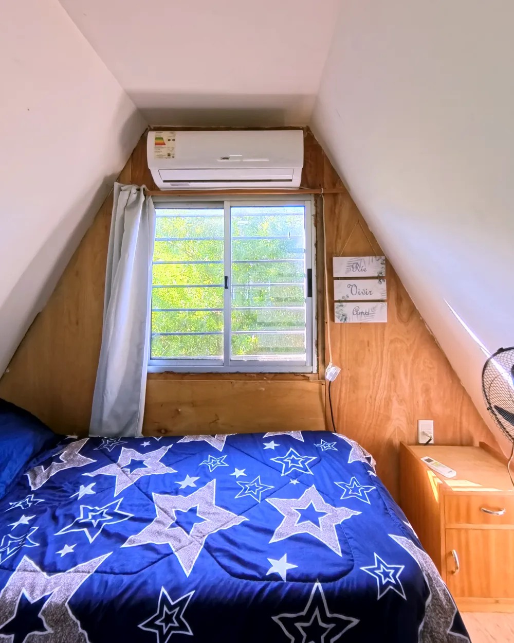 Dormitorio bajo el techo a dos aguas, con aire acondicionado y ventana a los árboles