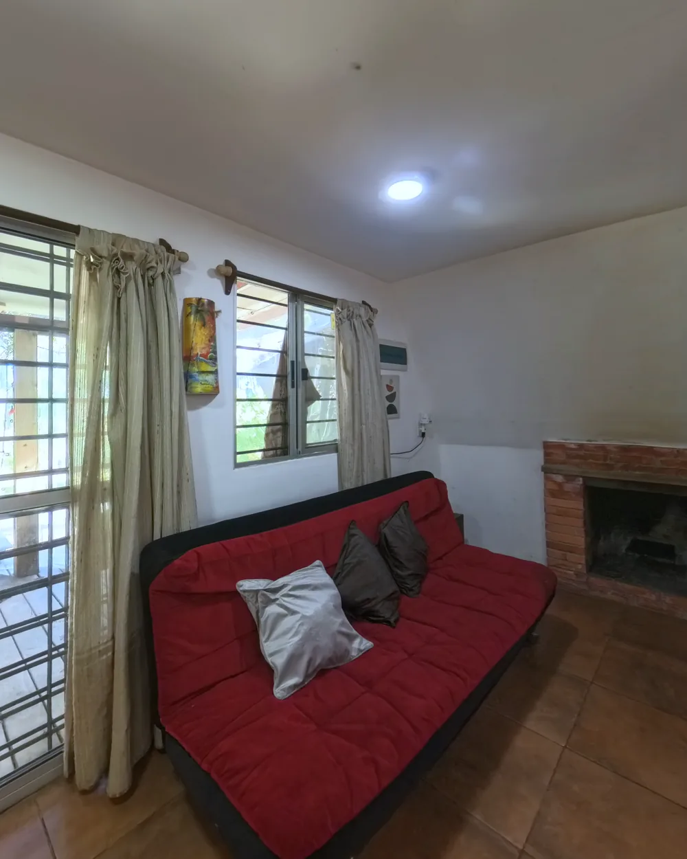 Living con sofá rojo, estufa a leña de ladrillo y ventanas a la barbacoa