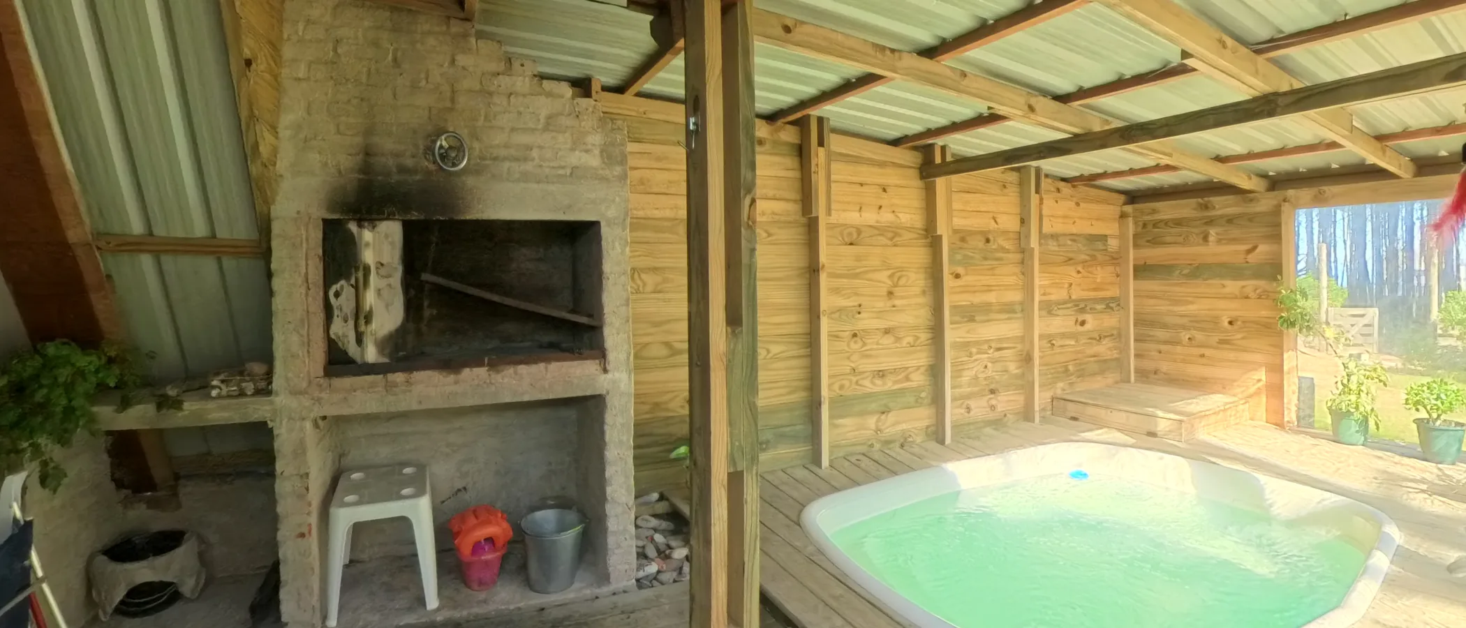 Piscina climatizada y techada, con el parrillero al lado y los pinos de fondo